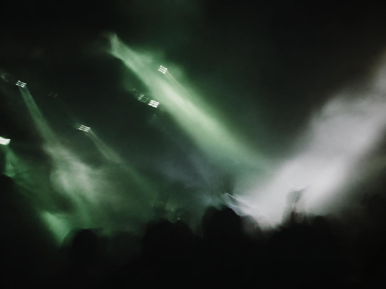 Blurred stage lights cutting through smoke above a crowd in green and white tones